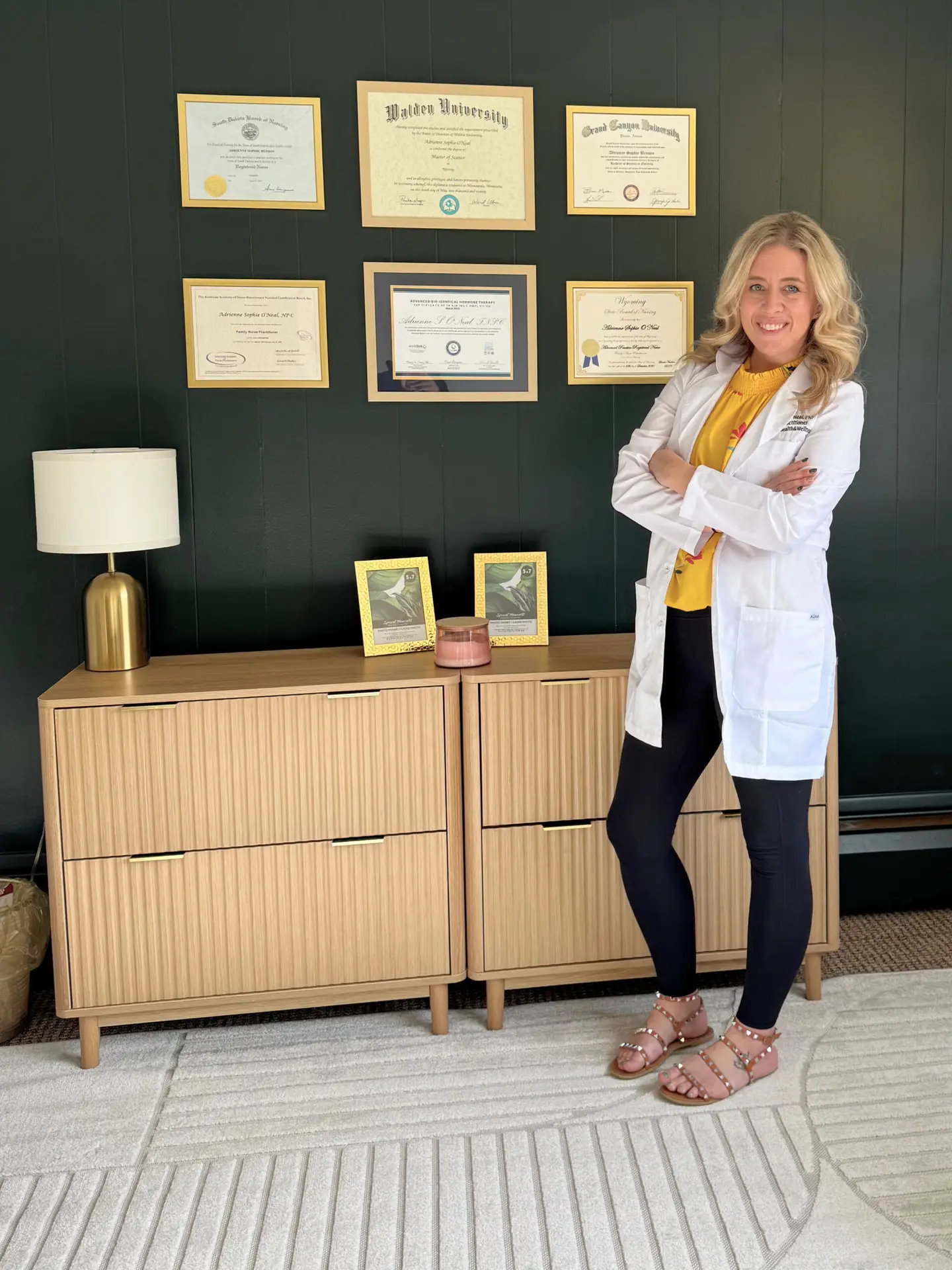 adrienne s. o’neal fnp-c standing in her office with framed medical diplomas on the wall, wearing a white coat and smiling confidently