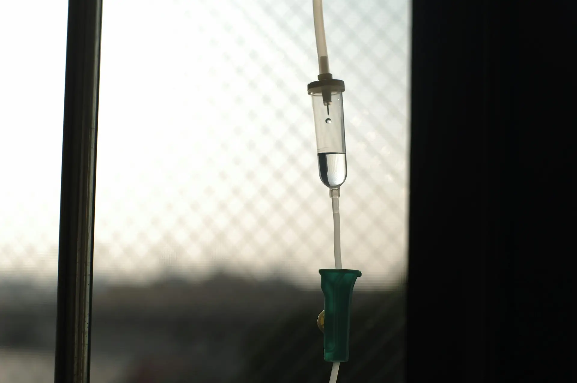 close-up of an iv drip chamber with fluid against a softly blurred window background