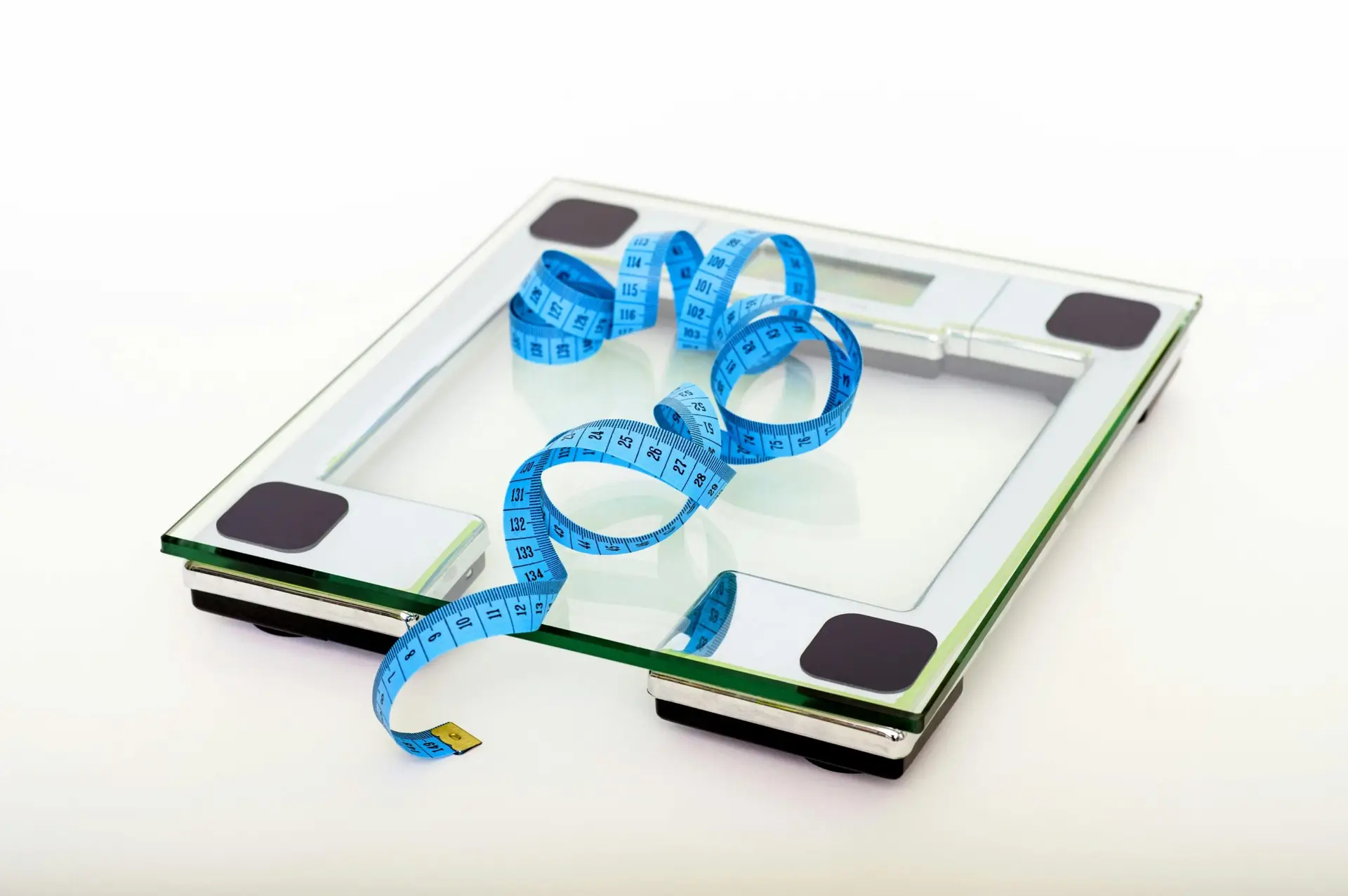 glass bathroom scale with a blue measuring tape coiled on top, symbolizing weight management and wellness